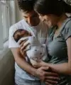 Een jonge mama en papa die hun pasgeboren baby vasthouden en er glimlachend naar kijken